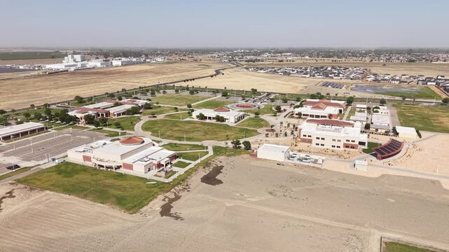Drone view zooming out to reveal the expansive campus of Lemoore College, revealing academic buildings, green spaces, and the surrounding flat, rural landscape of Central California