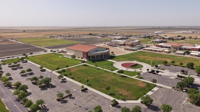 Rising drone view showing the campus and parking lot of Lemoore College in Lemoore, California, surrounded by the agricultural fields of the San Joaquin Valley on a clear day