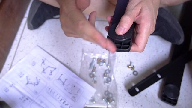 Male hands adjusting a black plastic leveling glider to repair and stabilize a furniture frame. Concept of home maintenance and DIY improvement.