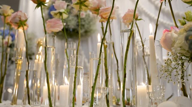 A table arranged with candles and flowers. The setup has tall glass vases with roses and lit candles. It creates a beautiful atmosphere for the event.