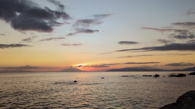 Panoramic static wide shot of the sea at sunset in Catanduanes, Bicol, with calm water, scattered rocks, and a glowing horizon