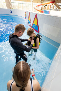 Scuba diving instructor helping a teenage boy adjust his equipment in an indoor swimming pool