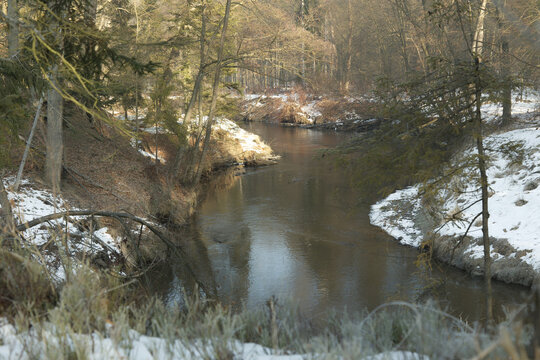 Flusslauf im Winterwald bei Sonnenaufgang mit Schnee am Ufer