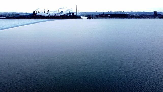 Aerial moving forward over Hamilton Harbour. Industrial sector of Hamilton, Ontario, Canada with factory smokestacks. Shot on a cold, cloudy, winter February afternoon with a slight high contrast.