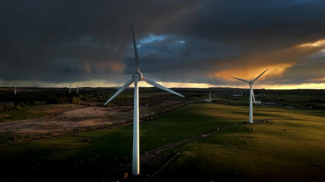Drone footage flying near wind turbines over rural fields and moorland under dark evening clouds in Scotland.