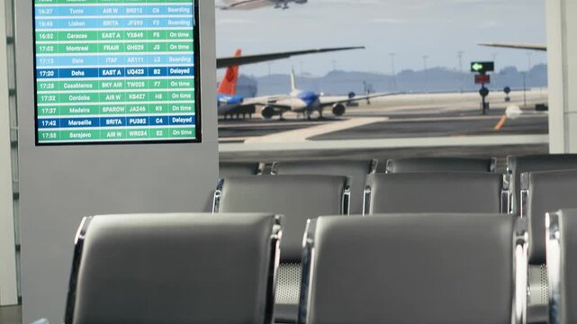 A quiet airport waiting area with empty seats, a partial departures display and aircraft visible beyond the terminal windows.