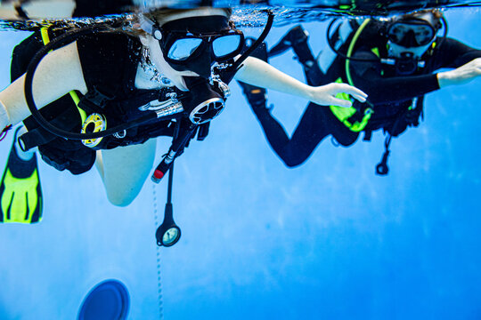 Close-up underwater view of a student and instructor scuba diving in a swimming pool during a training lesson