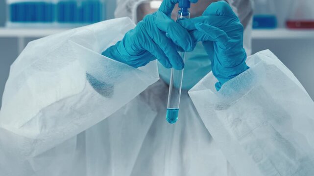 A researcher wearing full protective gear carefully examines a test tube containing blue solution in a sterile lab environment. The image highlights scientific progress and safety protocols