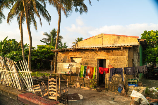 View of a modest weathered stone house with laundry hanging on a line and palm trees under a clear sky in Galle, Southern Province, Sri Lanka.