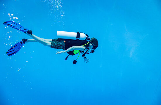 Scuba diver descending in a deep blue swimming pool