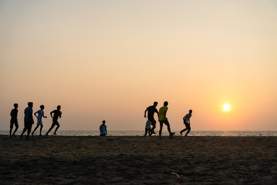 View of silhouettes of young men playing football on a sandy beach at sunset with the sun glowing over the ocean horizon Galle, Southern Province, Sri Lanka.