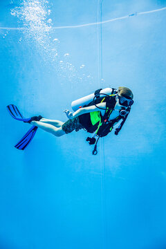 Scuba diver descending in a deep blue swimming pool