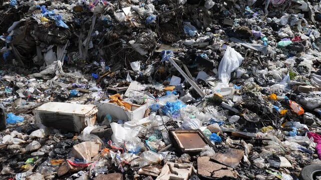 Trash piles up at a municipal landfill. Various types of waste are visible under sunlight. This shows the state of waste management in the area