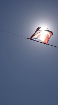 A string of Puerto Rican flags waving in the wind against a clear blue sky with sun rays.

