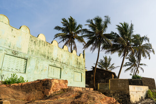 View of a weathered light green building with a scalloped roofline and palm trees against a clear blue sky in Galle, Southern Province, Sri Lanka.