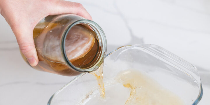 Pouring kombucha liquid with visible scoby from jar for fermentation tutorial background and recipe guide