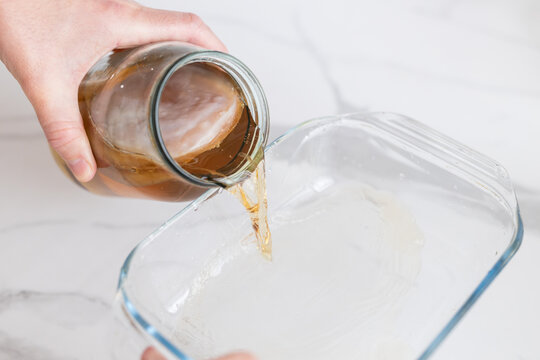 Pouring kombucha liquid with visible scoby from jar for fermentation tutorial background and recipe guide
