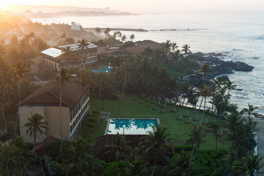 View of a luxury coastal resort with swimming pools and palm trees along the rocky shoreline at sunset in Galle, Southern Province, Sri Lanka.