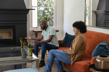 Fototapeta premium Diverse male friends chatting in living room on orange sofa and low chair near beer bottles
