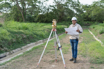 Obraz premium Surveyor reviewing plans operating a total station for land mapping