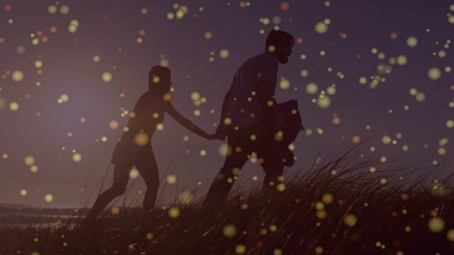 Sunset urging couple holding hands walking up dune with golden bokeh drifting in front for travel