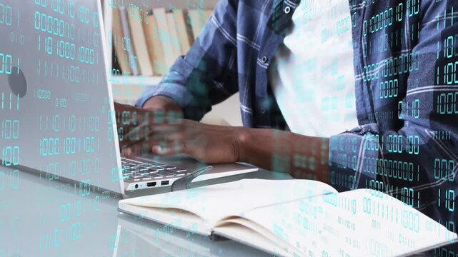 Man typing on laptop launching teal binary overlay across desk while checking notebook for code