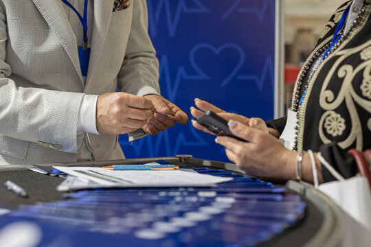 Medical Conference Registration and Payment Desk. Close-up of people exchanging a card and using a smartphone at a medical event registration table with paperwork.