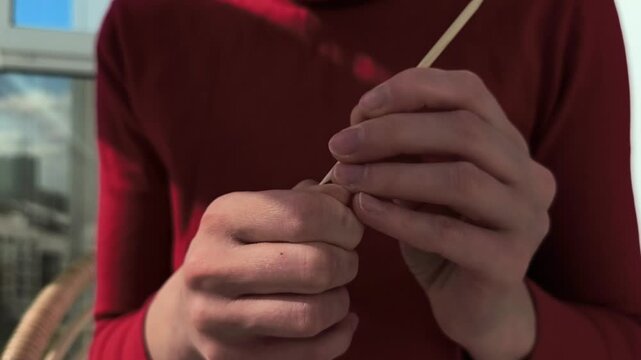 Hands use a wooden cuticle stick for fingernail care in close up. The manicure routine continues with precise grooming on natural nails. Personal hygiene and beauty maintenance at home..