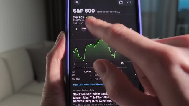Hand scrolls smartphone stock chart with SP 500 data. The screen shifts through monthly and long term market performance in close up. Mobile finance analysis and trading research concept..
