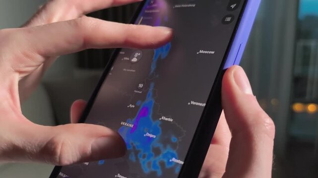 Hands use a smartphone weather map in close up. The screen shifts across Europe and Ukraine with forecast layers and location markers. Mobile climate tracking and travel planning concept..