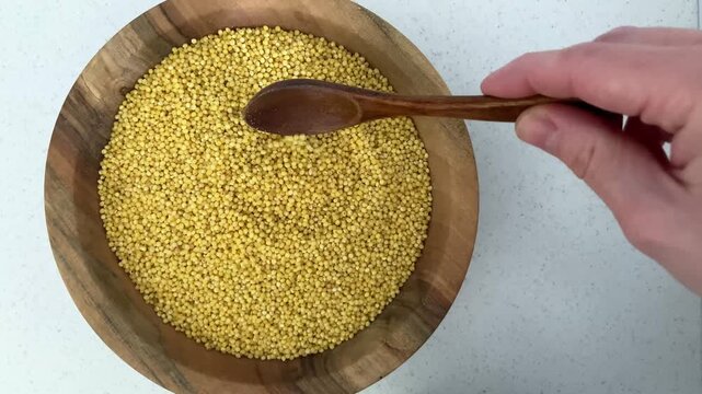 The woman pours the millet with a spoon, preparing it for cooking a safe and healthy dish. The topic of celiac disease and the need for careful selection of gluten-free foods