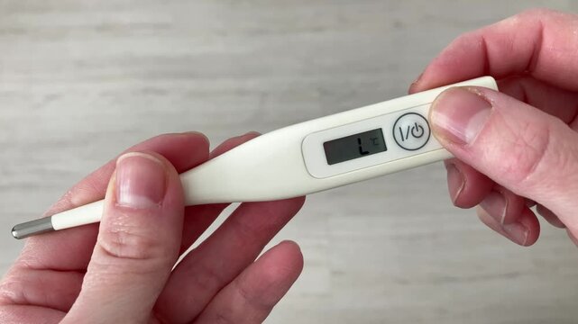 A woman holds a thermometer in her hand, ready to measure the temperature. Flu symptoms, severe weakness and malaise. Top view, close up