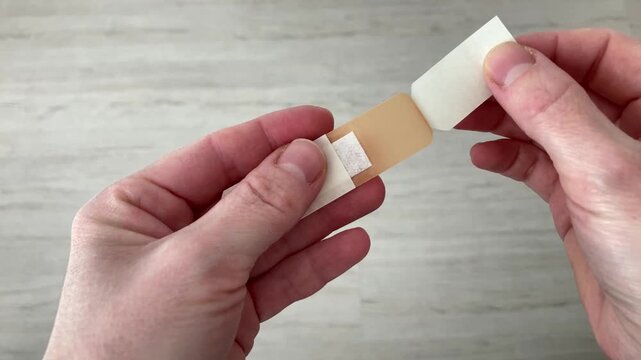 A woman opens a package with a Band-Aid. Using a patch for a small cut speeds up the healing process and reduces the risk of infection. Top view, close up