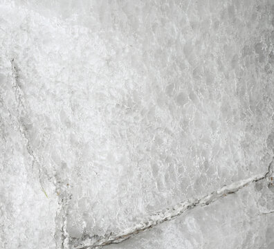 Horizontal close up of a weathered salt boulder surface with white and light gray crystalline halite texture, two large cracks, angular fracture lines, dirt specks, and natural debris