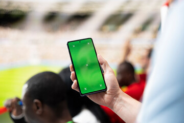 Fototapeta premium Excited football fans gather near a green screen phone mockup in stadium tribune for screen replacement and compositing.
