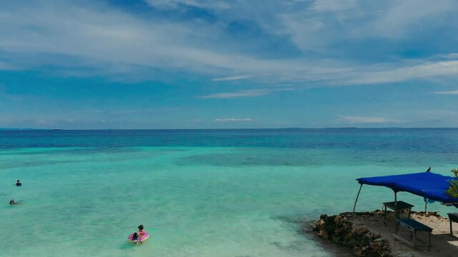 Drone rising shot from Isla Mucura beach looking at ocean then tilting down to show child with adult boy with aunt and grandfather swimming in crystal clear Caribbean water