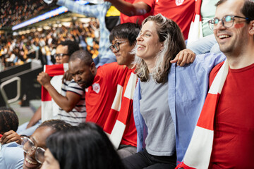 Fototapeta premium Passionate soccer fans gathered in the stadium stands during football match surrounded by loud crowd cheering and chanting. Diverse supporters with face paint show pride and strong team spirit.
