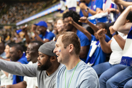 Soccer fans cheering and clapping during football match in stadium stands, exciting championship tournament. Supporters screaming loudly for the home team, fan chants for team spirit.