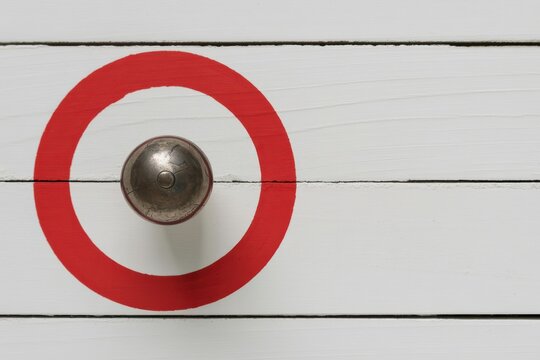 A metal knob is centered within a red circle on a white wooden panel background.