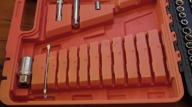 Tools are organized in a tool case with various sizes and types on a wooden surface in a garage setting, a man's hand stacking wrenches