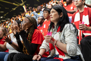 Obraz premium Red team football supporters reacting with anxious gestures in stadium stands during tense live soccer match, scarves and crowd emotion. Fans with clenched fists during crucial moment in the match.