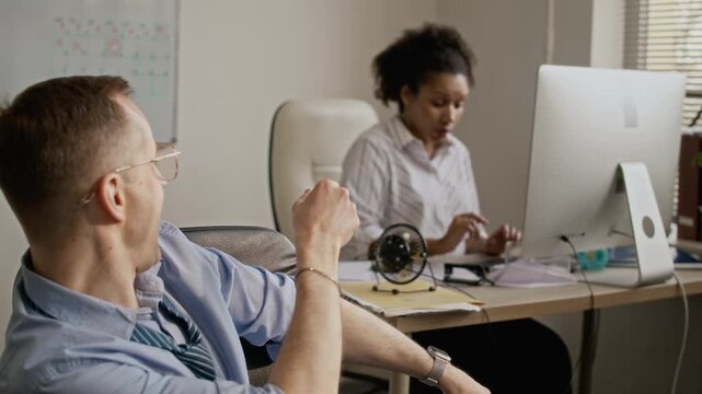 Handheld shot of Caucasian man breaking into wide smile while creating paper airplane and launching it, his African American colleague smiling and laughing while catching it