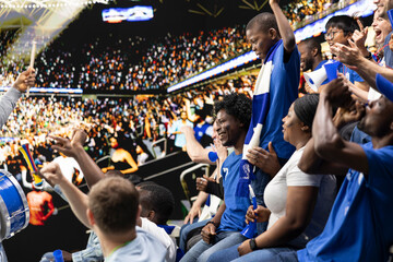 Fototapeta premium Black parents enjoying quality family time at football stadium, cheering for blue team during intense soccer match. Family sharing excitement of live sports with child fan, role model.