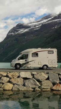 Motorhome parked by mountain lake in dramatic alpine landscape, vertical travel scene.