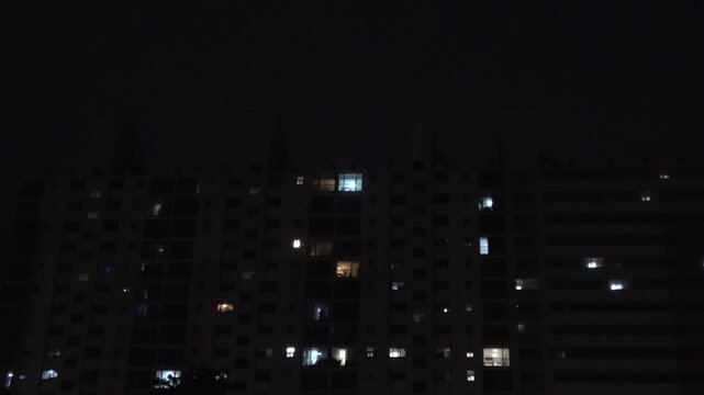 Dark apartment building at night with sparse lights and a motion sensor light turning on, 4K