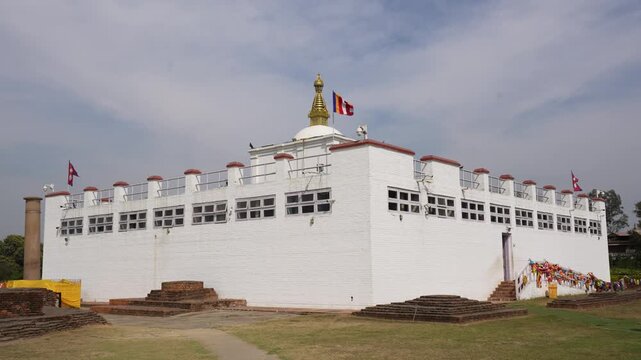 Lumbini, Nepal - 15 January 2024: View of the white Maya Devi Temple building, the birthplace of Lord Buddha, with prayer flags and ancient ruins under a bright sky.