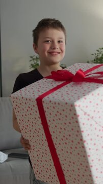 Child happily carrying large gift box, showcasing excitement and joy in a cozy indoor setting with modern decor