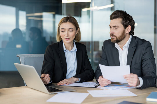 Business people working together, discussing data and ideas while using a laptop and reviewing documents, showcasing teamwork and professional cooperation in an office setting