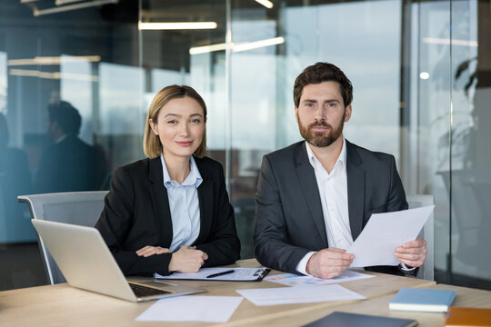 Business partners at an office desk review documents and a laptop during a focused meeting, discussing strategy, planning projects and finalizing a professional agreement