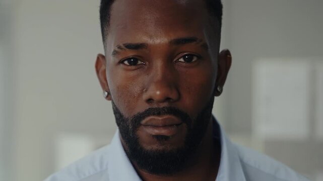 Portrait of serious African American businessman in casual attire stands in office closeup. Man entrepreneur with tranquil facial expression in corporate space
